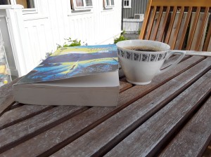 Kaffekopp og bok på et bord. Det ble en del kaffe og lesing på terrassen i sommer. Det begeistrer.